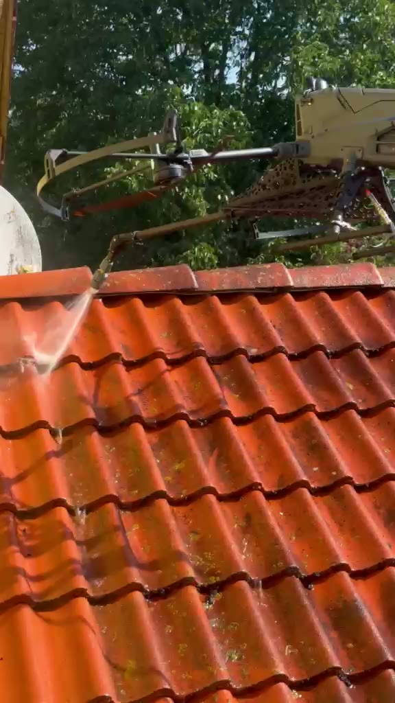 Reinigungsdrohne sprüht Wasser über ein bemoostes rotes Ziegeldach