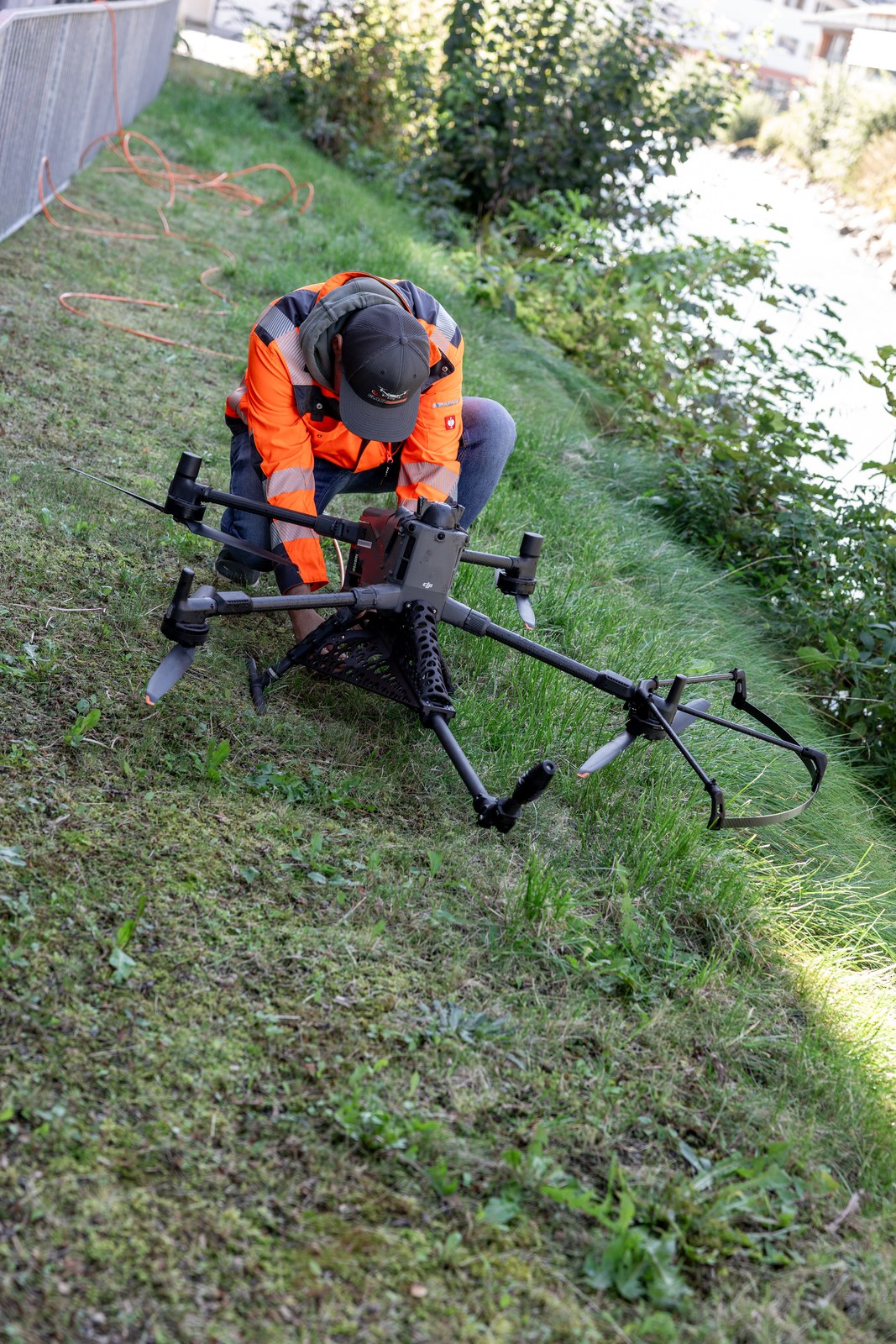 Teammitglied kniet im Gras und bereitet die Reinigungsdrohne mit Sprühlanze vor